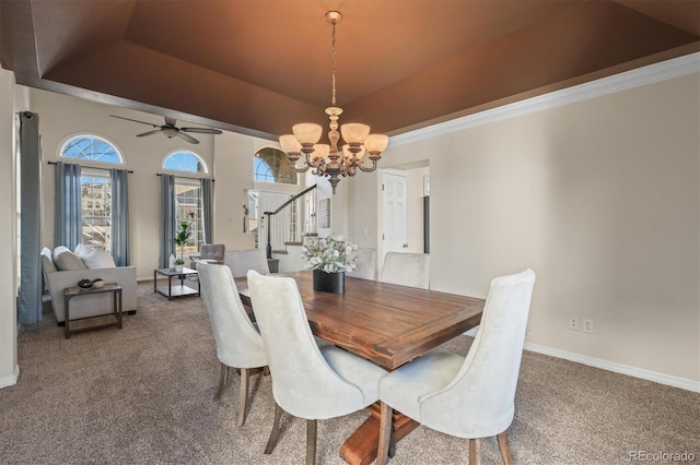 dining room with ceiling fan with notable chandelier, carpet floors, stairs, a raised ceiling, and baseboards