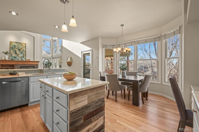 kitchen featuring an inviting chandelier, light wood-style flooring, a kitchen island, dishwasher, and a sink