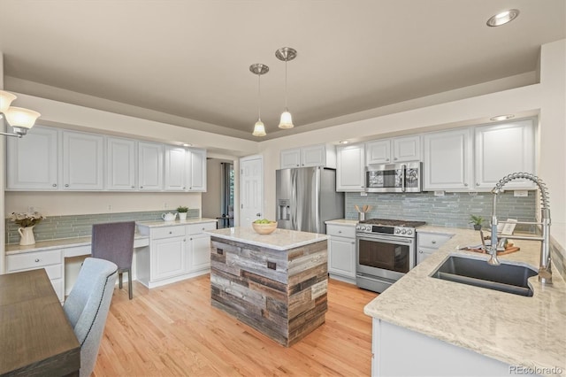 kitchen featuring light wood-style flooring, light stone countertops, appliances with stainless steel finishes, a sink, and hanging light fixtures
