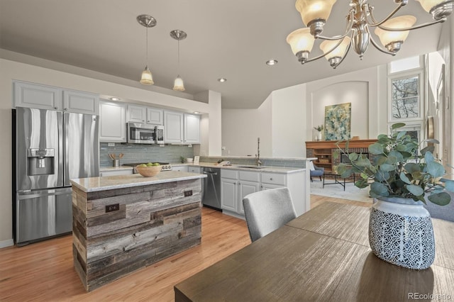 kitchen with an inviting chandelier, light wood-type flooring, a peninsula, stainless steel appliances, and backsplash
