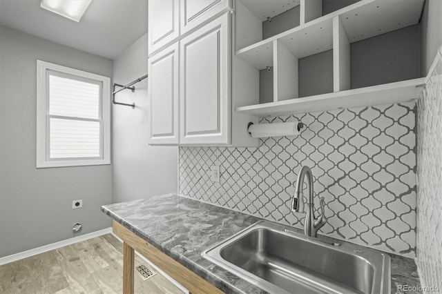 kitchen with open shelves, white cabinets, a sink, light wood finished floors, and backsplash