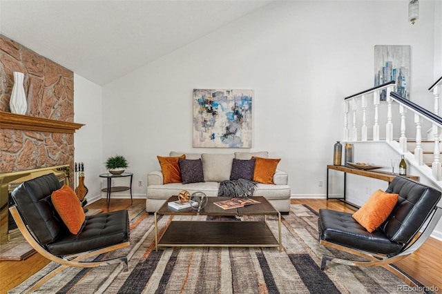 living room featuring high vaulted ceiling, hardwood / wood-style flooring, and a stone fireplace