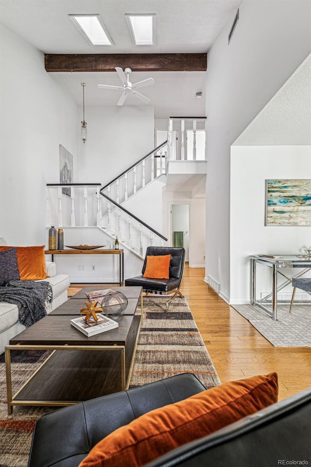 living room with ceiling fan, beamed ceiling, a skylight, hardwood / wood-style flooring, and a towering ceiling