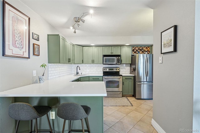 kitchen with a kitchen bar, sink, green cabinets, stainless steel appliances, and decorative backsplash