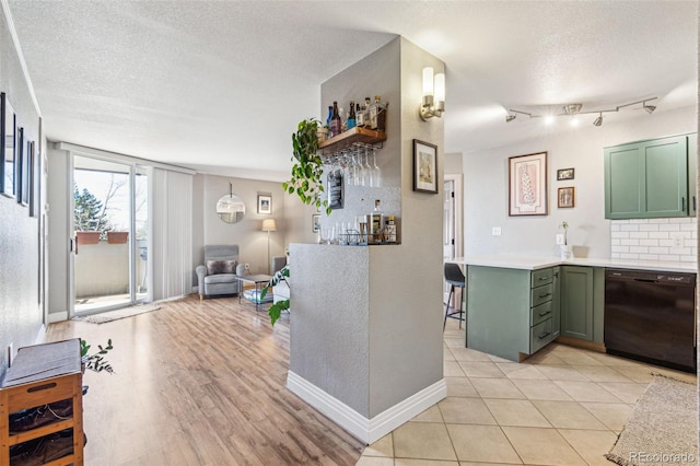 interior space featuring tasteful backsplash, dishwasher, green cabinets, and a textured ceiling