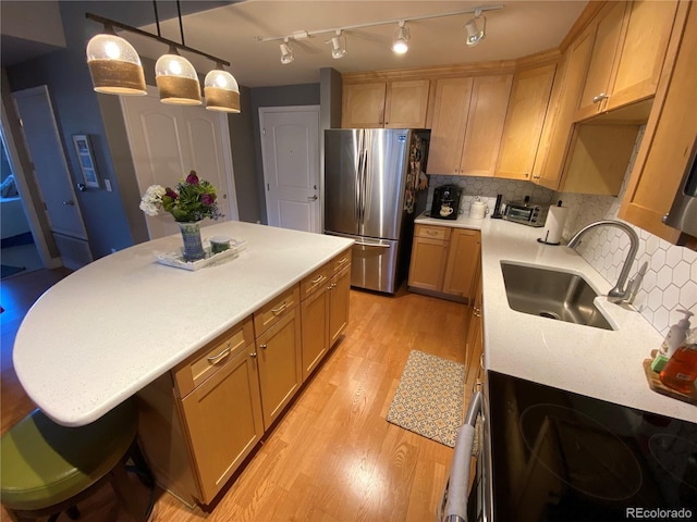 kitchen featuring hanging light fixtures, sink, light hardwood / wood-style flooring, tasteful backsplash, and stainless steel refrigerator