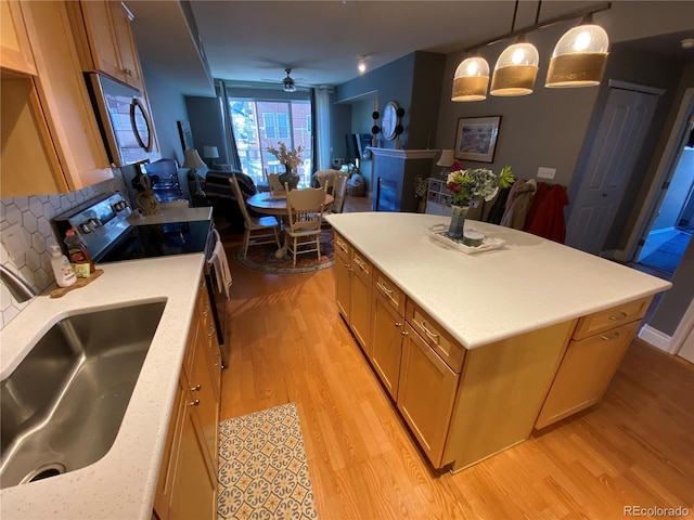 kitchen with sink, hanging light fixtures, ceiling fan, appliances with stainless steel finishes, and a kitchen island