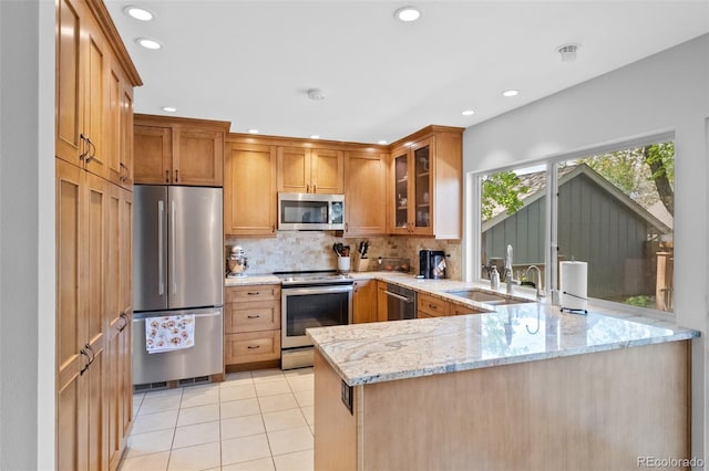 kitchen featuring appliances with stainless steel finishes, a sink, a peninsula, light stone counters, and glass insert cabinets