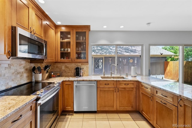 kitchen with stainless steel appliances, a sink, brown cabinets, tasteful backsplash, and recessed lighting
