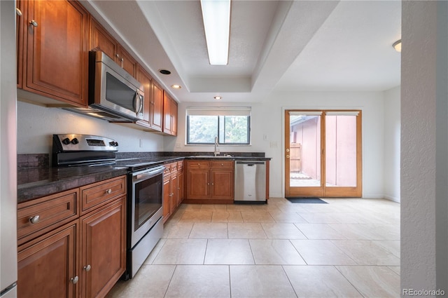 kitchen featuring appliances with stainless steel finishes, dark stone counters, sink, light tile patterned floors, and a tray ceiling