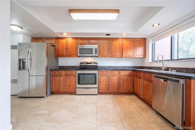 kitchen with sink, light tile patterned floors, a tray ceiling, and stainless steel appliances