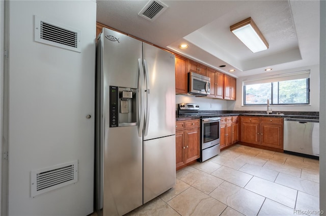 kitchen featuring sink, a raised ceiling, light tile patterned floors, and appliances with stainless steel finishes