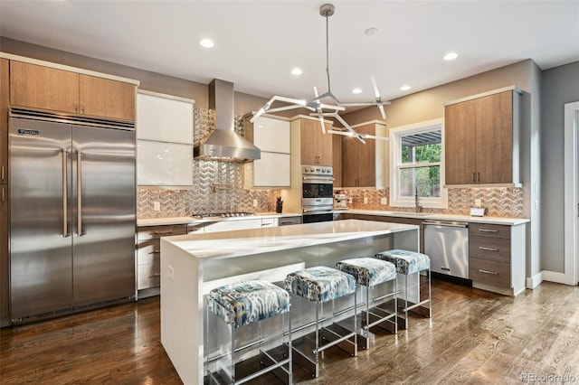 445 Forest St, Denver, CO 80220 - kitchen featuring appliances with stainless steel finishes, wall chimney range hood, light countertops, a kitchen bar, and recessed lighting