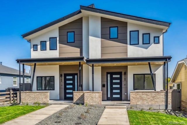 contemporary home featuring covered porch, stucco siding, fence, and brick siding