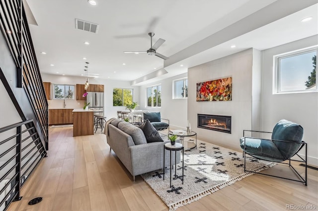 living room with a glass covered fireplace, light wood-style floors, visible vents, and a ceiling fan