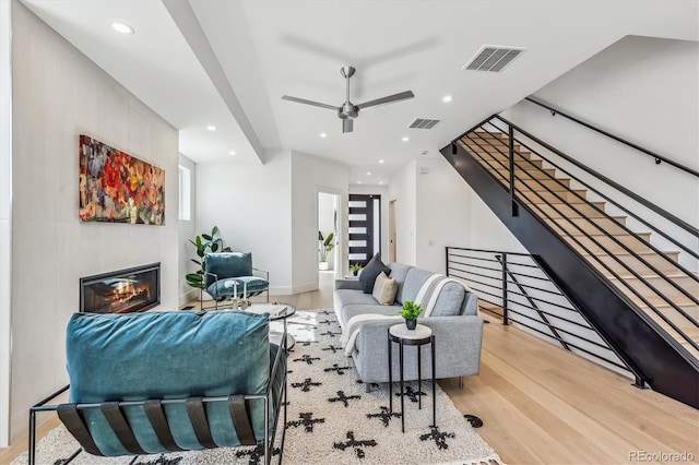 living area with a glass covered fireplace, recessed lighting, visible vents, ceiling fan, and wood finished floors