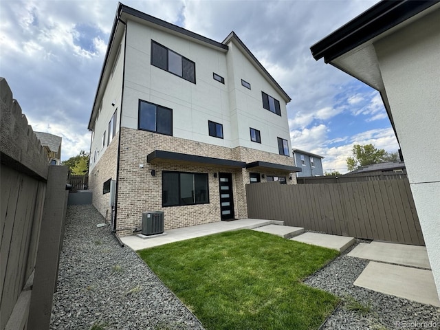 rear view of house featuring a patio, brick siding, a fenced backyard, central AC unit, and a yard