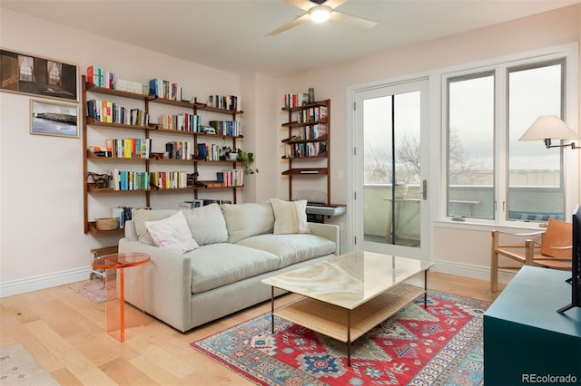 living area featuring baseboards, light wood-type flooring, and a ceiling fan