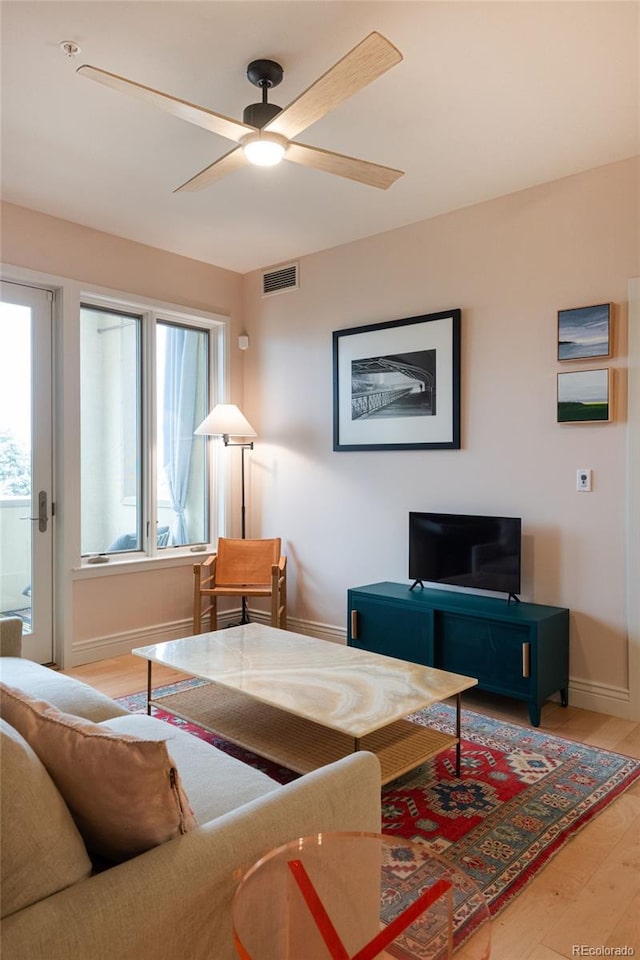 living area featuring visible vents, baseboards, a ceiling fan, and wood finished floors