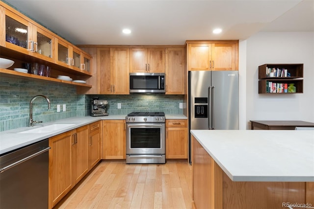 kitchen with light wood-type flooring, a sink, appliances with stainless steel finishes, light countertops, and decorative backsplash