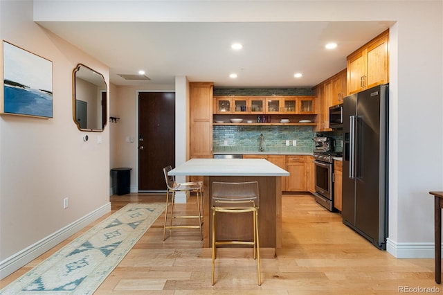 kitchen featuring light wood-style flooring, a sink, a center island, stainless steel appliances, and decorative backsplash