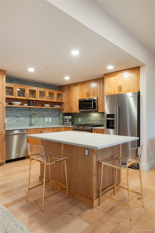 kitchen with a breakfast bar, a kitchen island, appliances with stainless steel finishes, light countertops, and glass insert cabinets