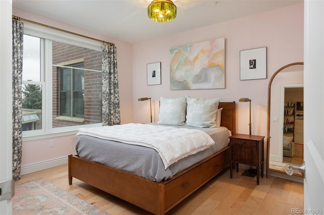 bedroom with baseboards, light wood-style floors, and arched walkways