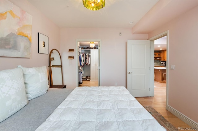 bedroom with a walk in closet, wood finished floors, a closet, and baseboards