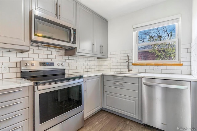 kitchen with a sink, appliances with stainless steel finishes, wood finished floors, and gray cabinetry