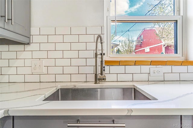 details featuring a sink, tasteful backsplash, light stone countertops, and gray cabinets