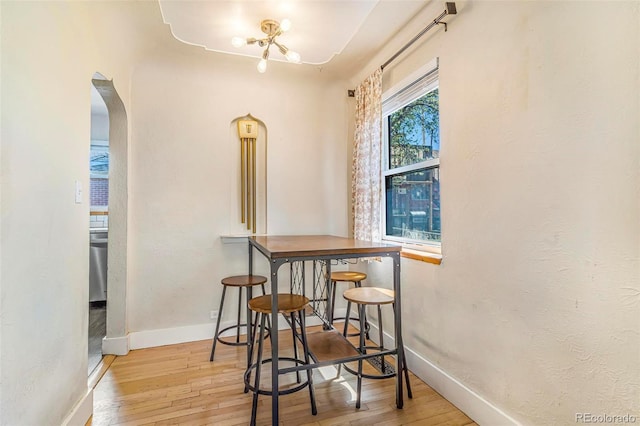dining room featuring arched walkways, baseboards, a notable chandelier, and hardwood / wood-style floors