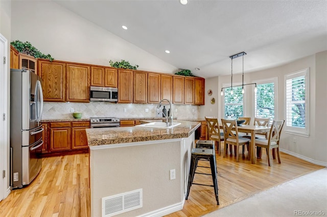 6633 E 166th Pl, Brighton, CO 80602 - kitchen featuring stainless steel appliances, a sink, brown cabinetry, vaulted ceiling, and tasteful backsplash