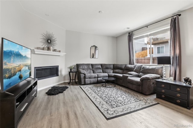 living area with a glass covered fireplace, baseboards, and wood finished floors