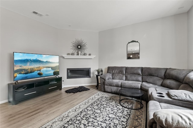 living room featuring a glass covered fireplace, visible vents, baseboards, and wood finished floors