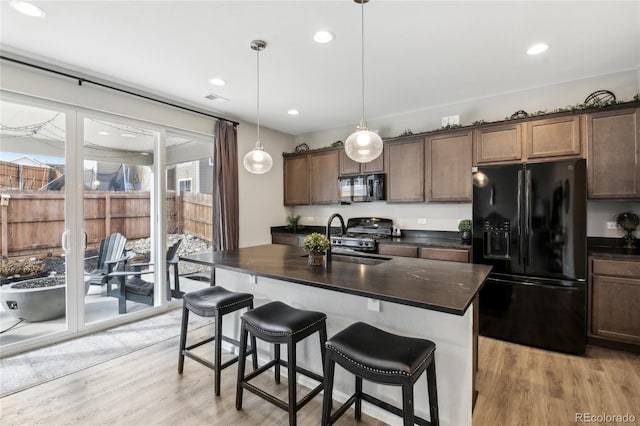 kitchen with black appliances, dark countertops, light wood-style floors, and a sink