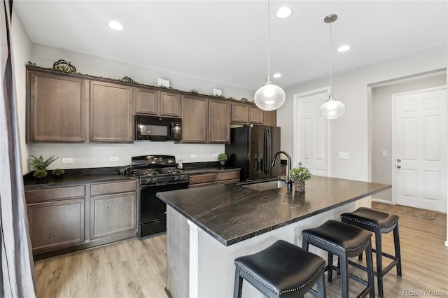 kitchen featuring black appliances, a sink, recessed lighting, a breakfast bar area, and light wood finished floors