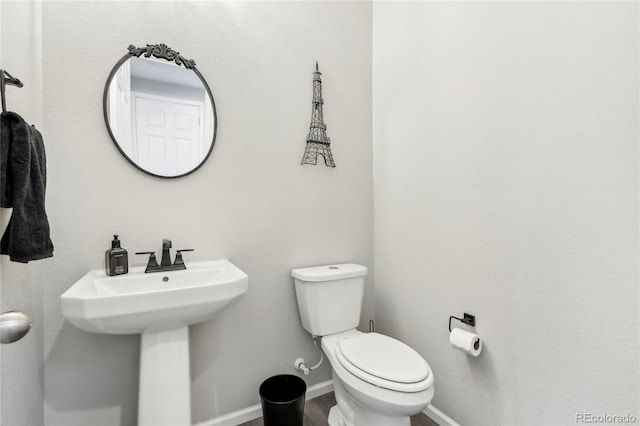 bathroom featuring toilet, wood finished floors, baseboards, and a sink