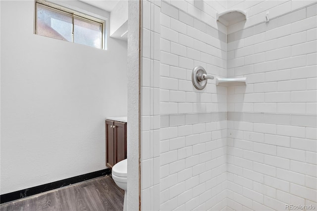 bathroom featuring toilet, hardwood / wood-style floors, and a tile shower