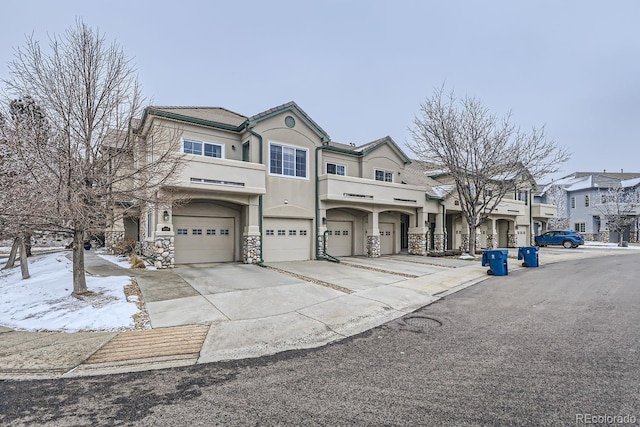 view of property with stucco siding, concrete driveway, an attached garage, a residential view, and stone siding