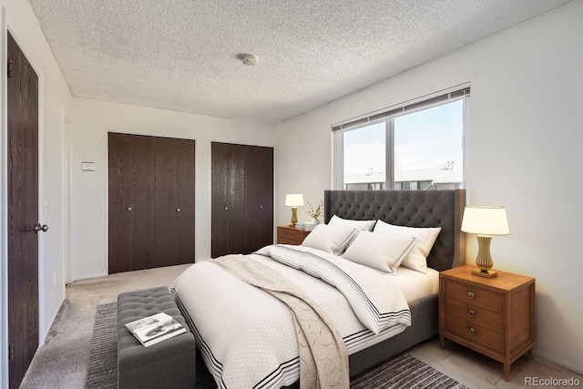 bedroom featuring light carpet, two closets, and a textured ceiling