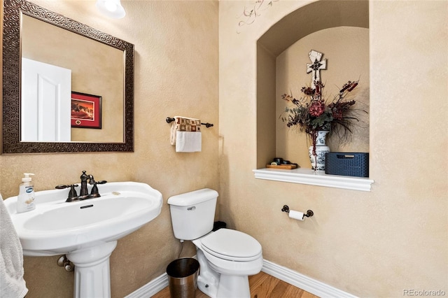 half bathroom featuring a sink, baseboards, toilet, and wood finished floors