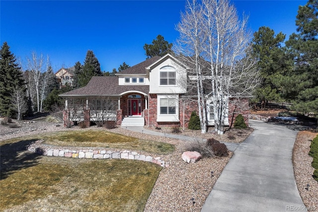 traditional home featuring a front yard, brick siding, driveway, and covered porch