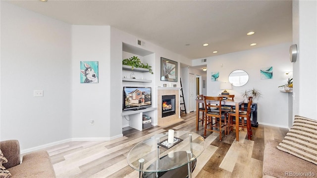 living room with built in features, a fireplace, and light hardwood / wood-style flooring