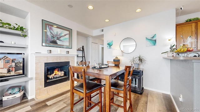 dining area with a tiled fireplace and light wood-type flooring