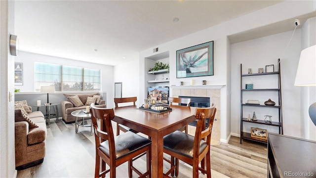 dining space with a tiled fireplace, built in shelves, and light hardwood / wood-style floors