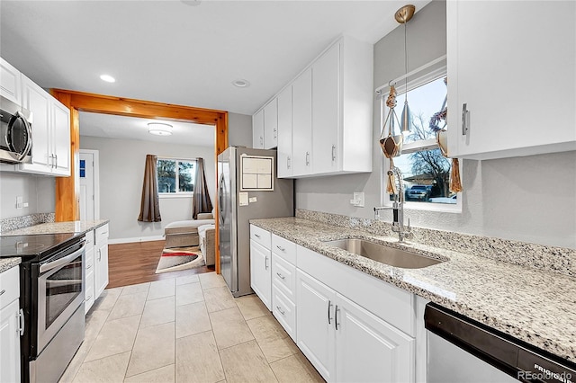 kitchen with light stone counters, stainless steel appliances, sink, pendant lighting, and white cabinets