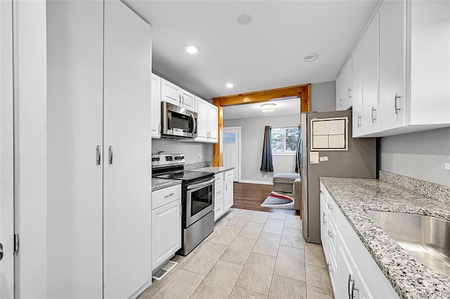 kitchen featuring appliances with stainless steel finishes, light stone counters, sink, white cabinetry, and light tile patterned flooring