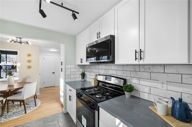 kitchen with appliances with stainless steel finishes, tasteful backsplash, white cabinets, light tile patterned floors, and track lighting