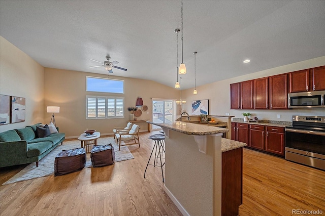 kitchen featuring a kitchen island with sink, stainless steel appliances, light hardwood / wood-style floors, a kitchen bar, and decorative light fixtures