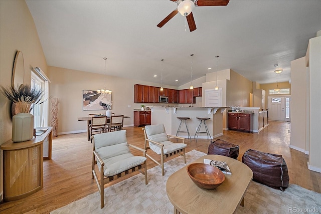 living room featuring lofted ceiling, ceiling fan with notable chandelier, and light hardwood / wood-style floors